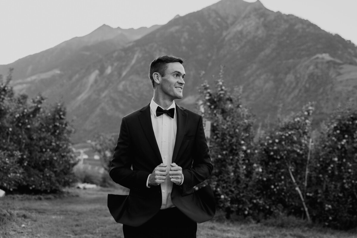 Groom standing in orchard with mountains behind him