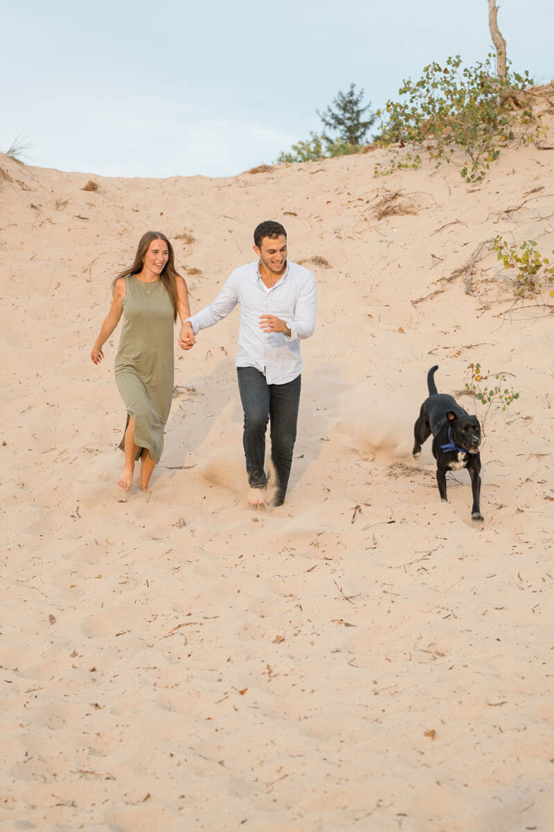 Couple runs down a giant sand dune with their dog