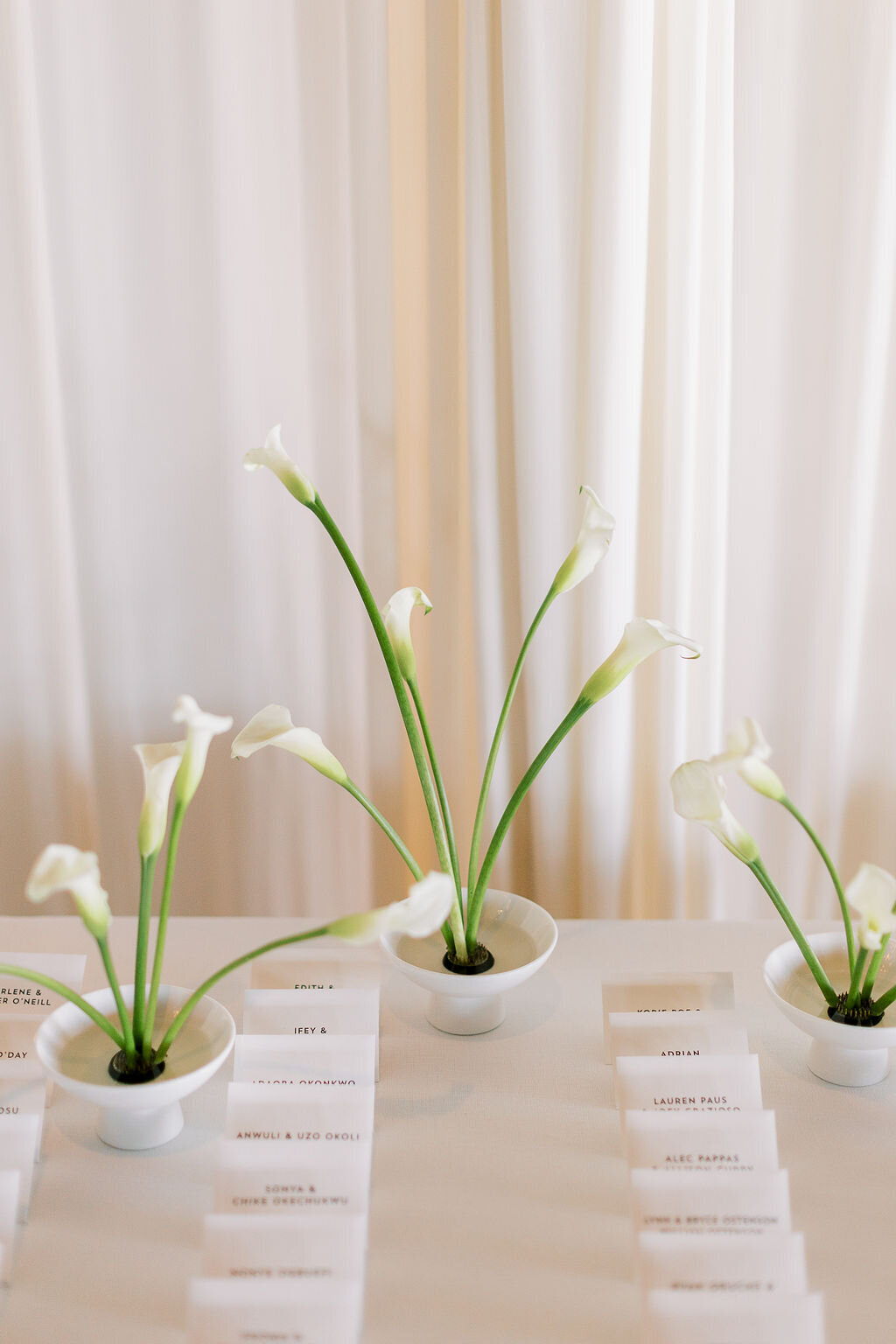 Elegant white place cards with guest names, accompanied by calla lilies in minimalist vases.