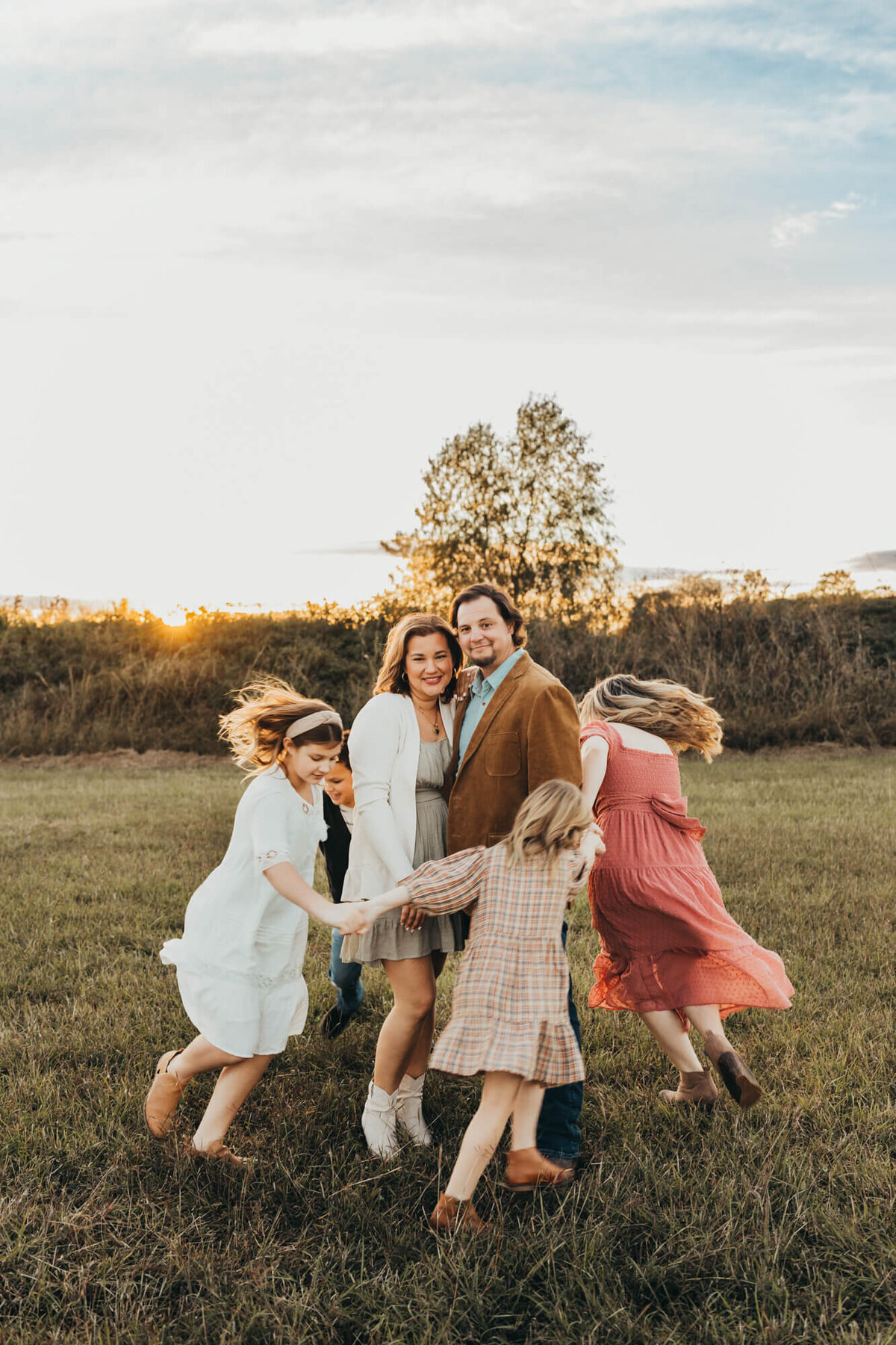 mom and dad stand still holding each other in middle of circle while their children run around them.