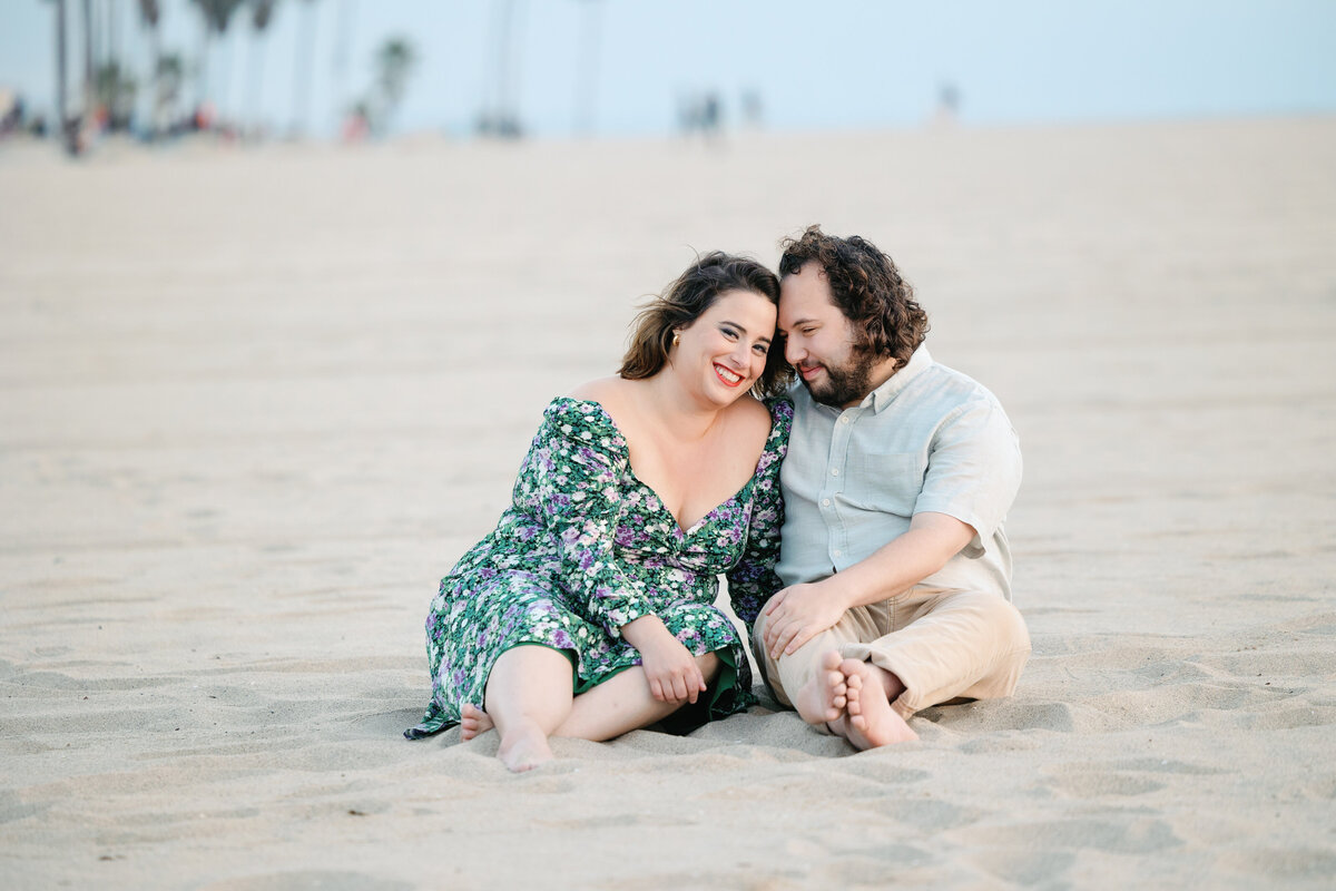 A couple sitting in the sand with their heads together