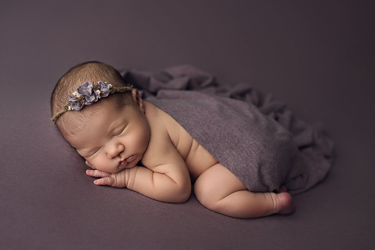 A New Orleans Newborn Photographer posed a newborn baby while sleeping in a purple blanket