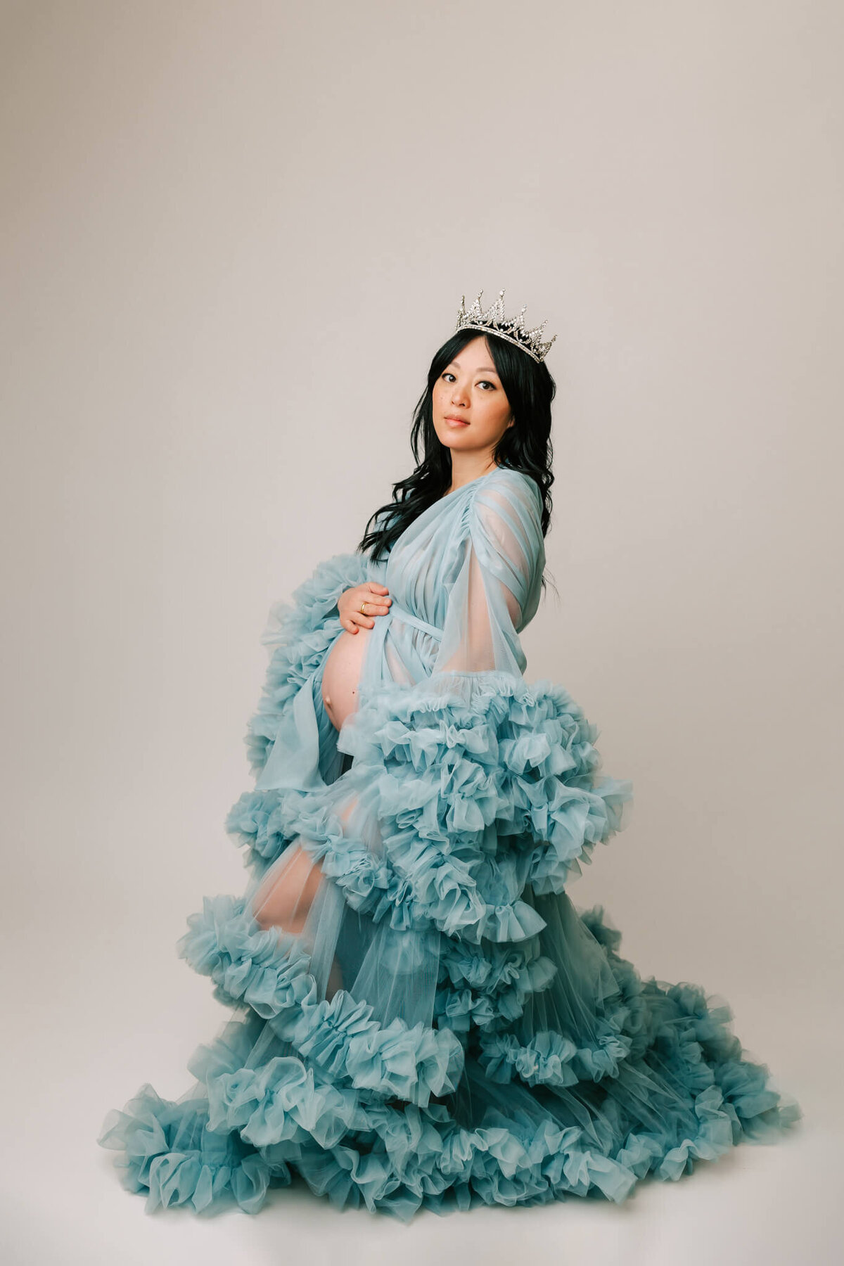 fine art maternity portrait of a mom wearing a blue tulle dress and crown. She is looking at the camera