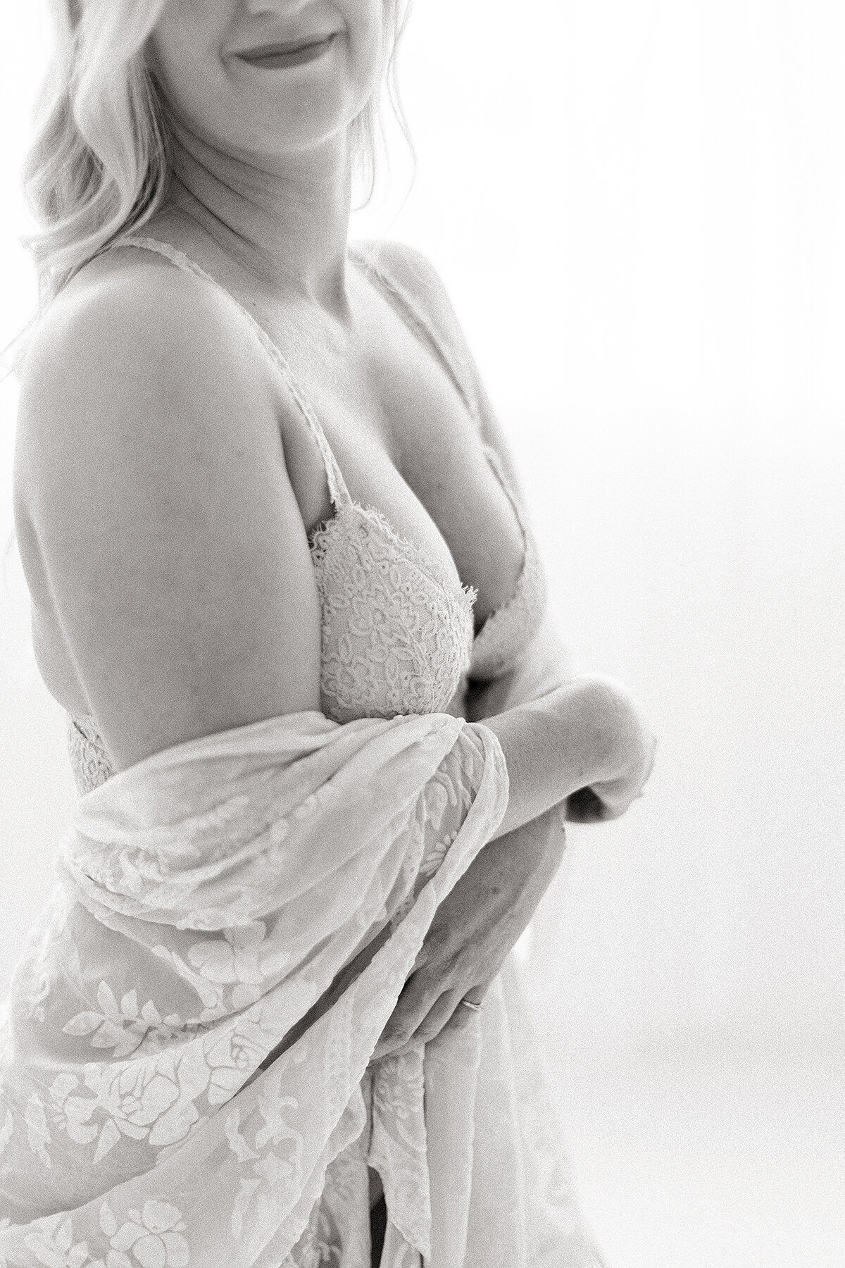 Close up black and white in studio boudoir photo of a woman wearing a lace bra with a robe draped and hanging off her shoulders.