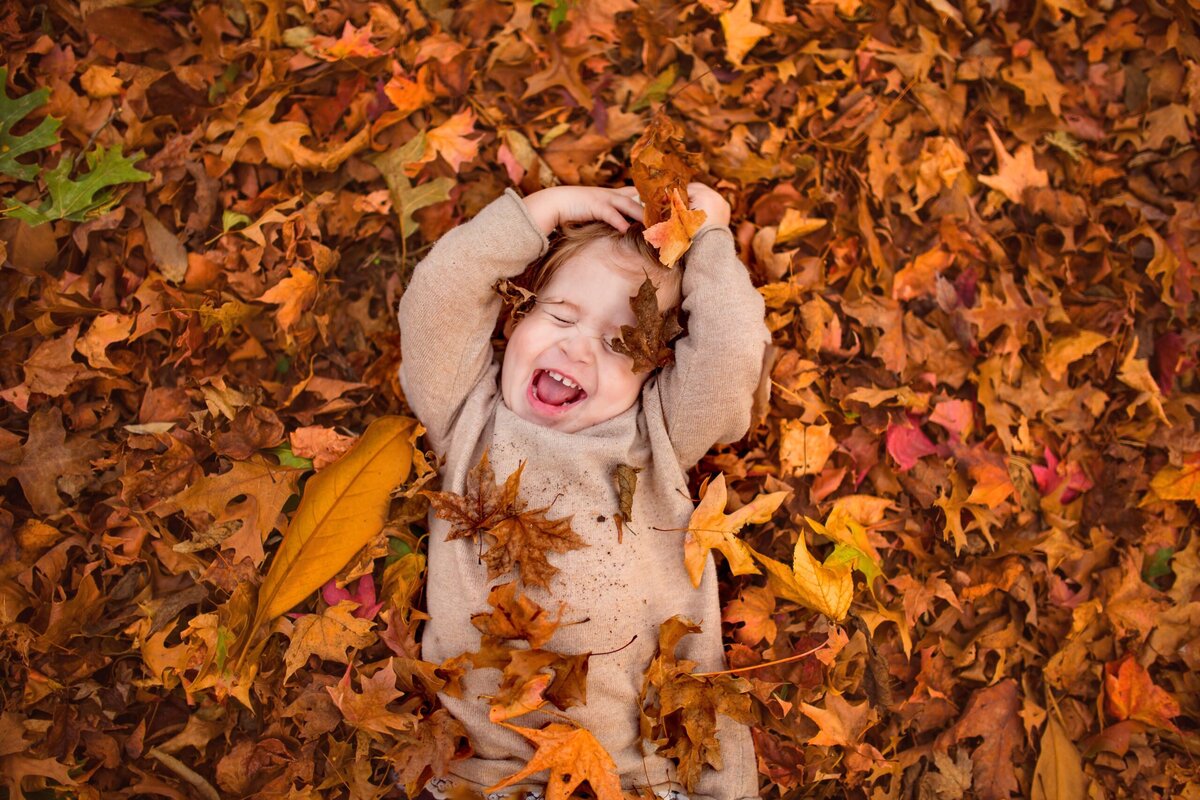 A young girl plays in the orange colored fall leaves.