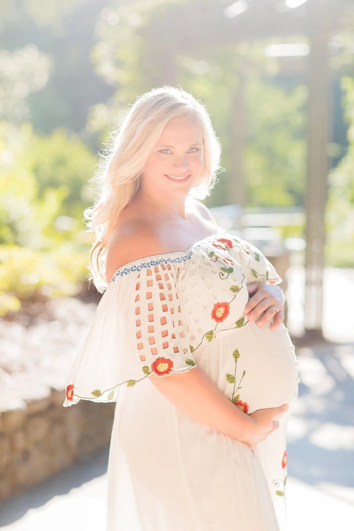 A woman in a dress with her hands around her pregnant stomach.