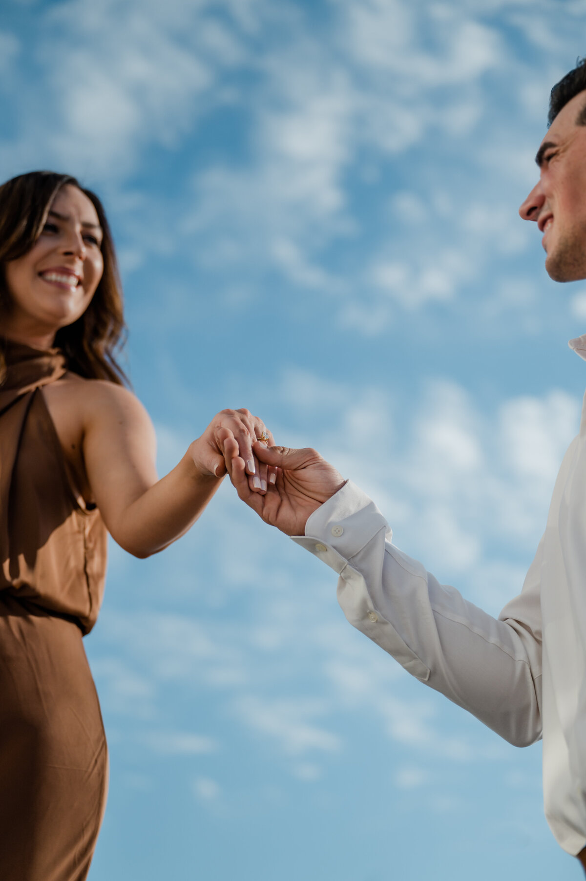 Engagement ring held up to the sky, sparkling against a dreamy cloud-filled backdrop.