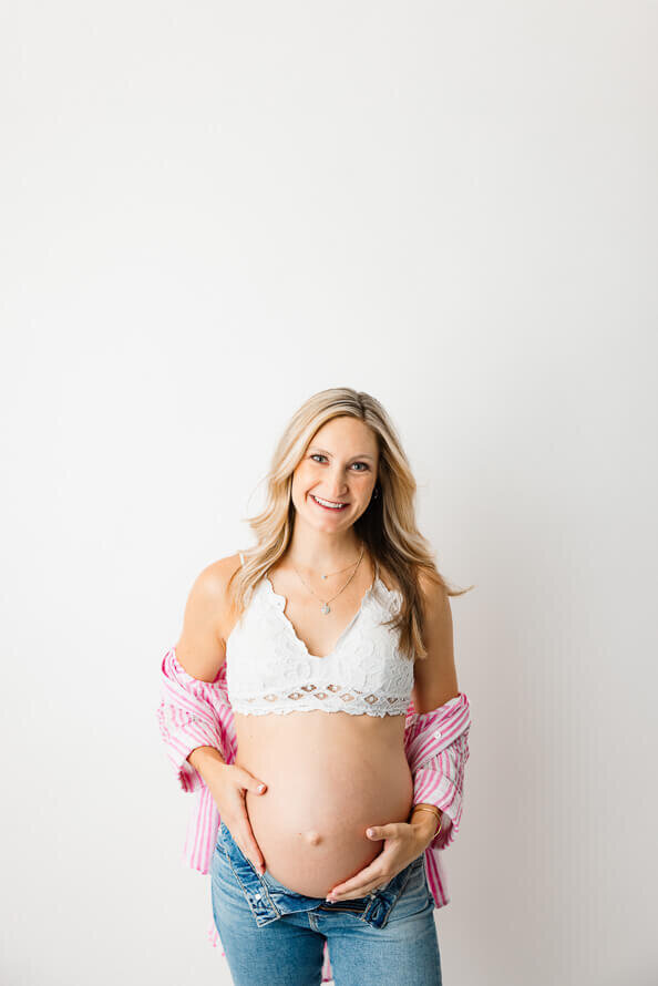 A woman looks and smiles at the camera, holding her pregnant belly.