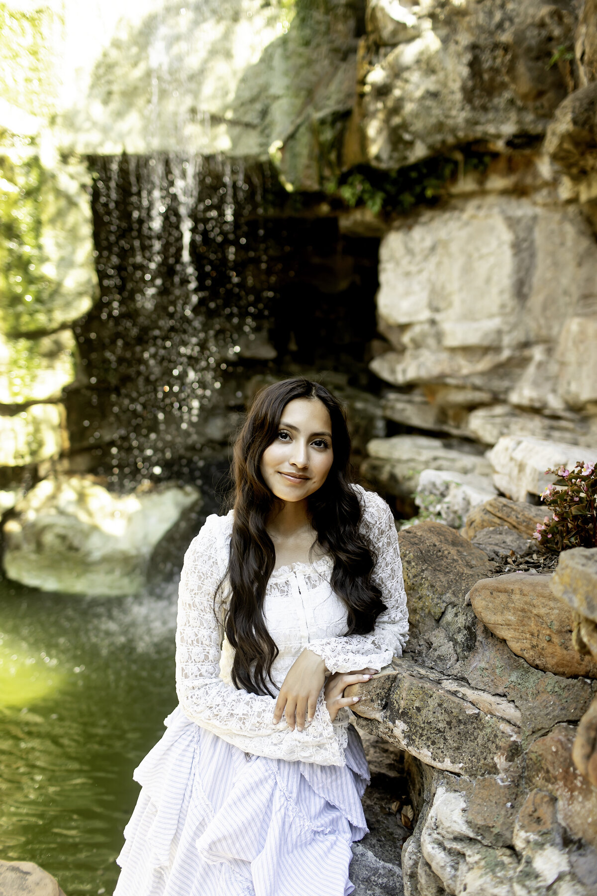 A high school senior in a light dress, standing by the peaceful water features at Chandor Gardens, Weatherford, TX, capturing a timeless and serene moment