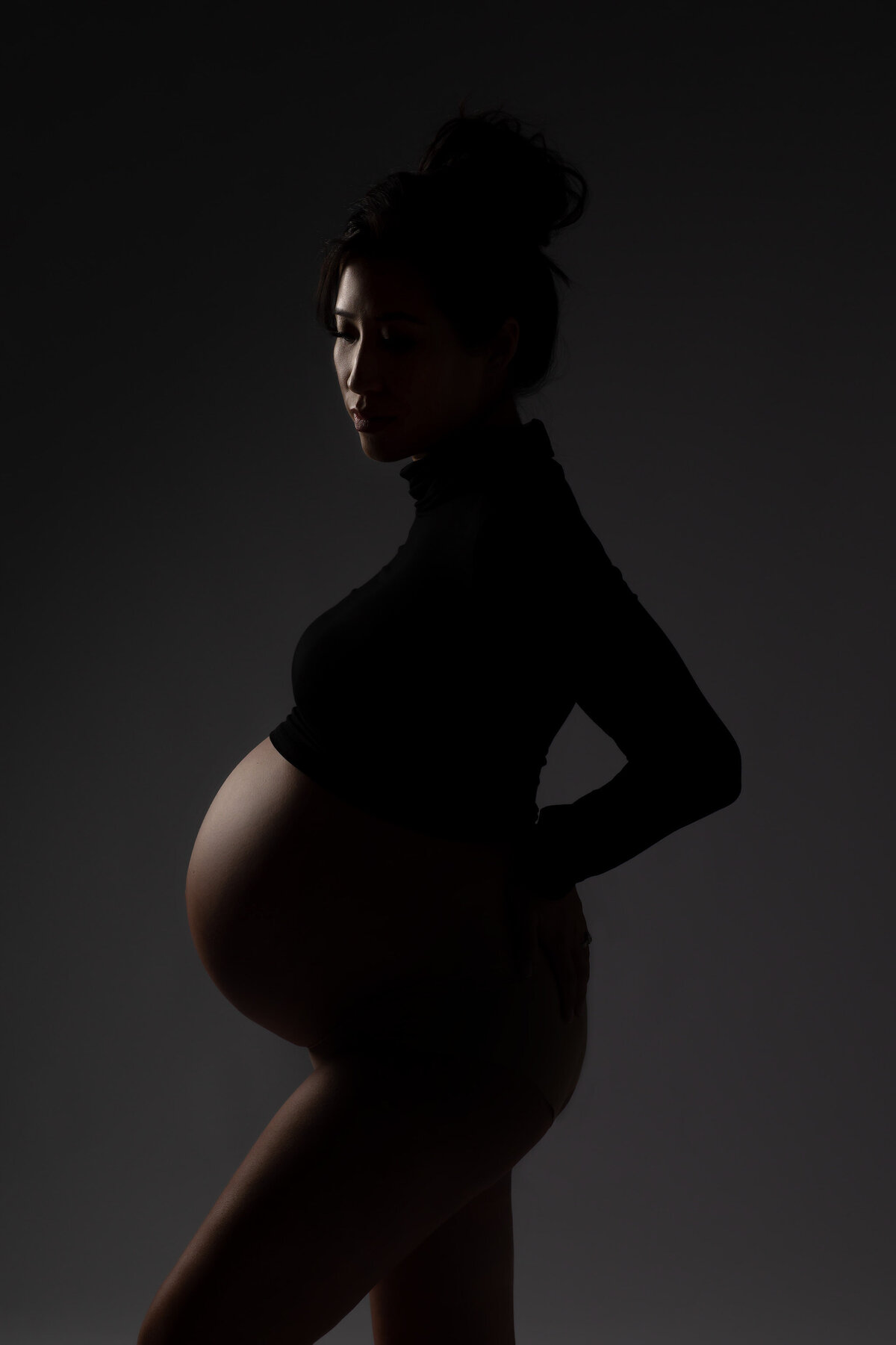 Dark and dramatic pregnancy image. The light just barely touching the silhouette of the woman's belly and face. Captured by DFW maternity photographer Lindsay Walden