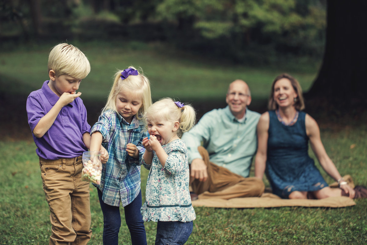 charlotte family photographer jamie lucido creates playful family portrait with children eating marshmallows and parents laughing at Latta Park