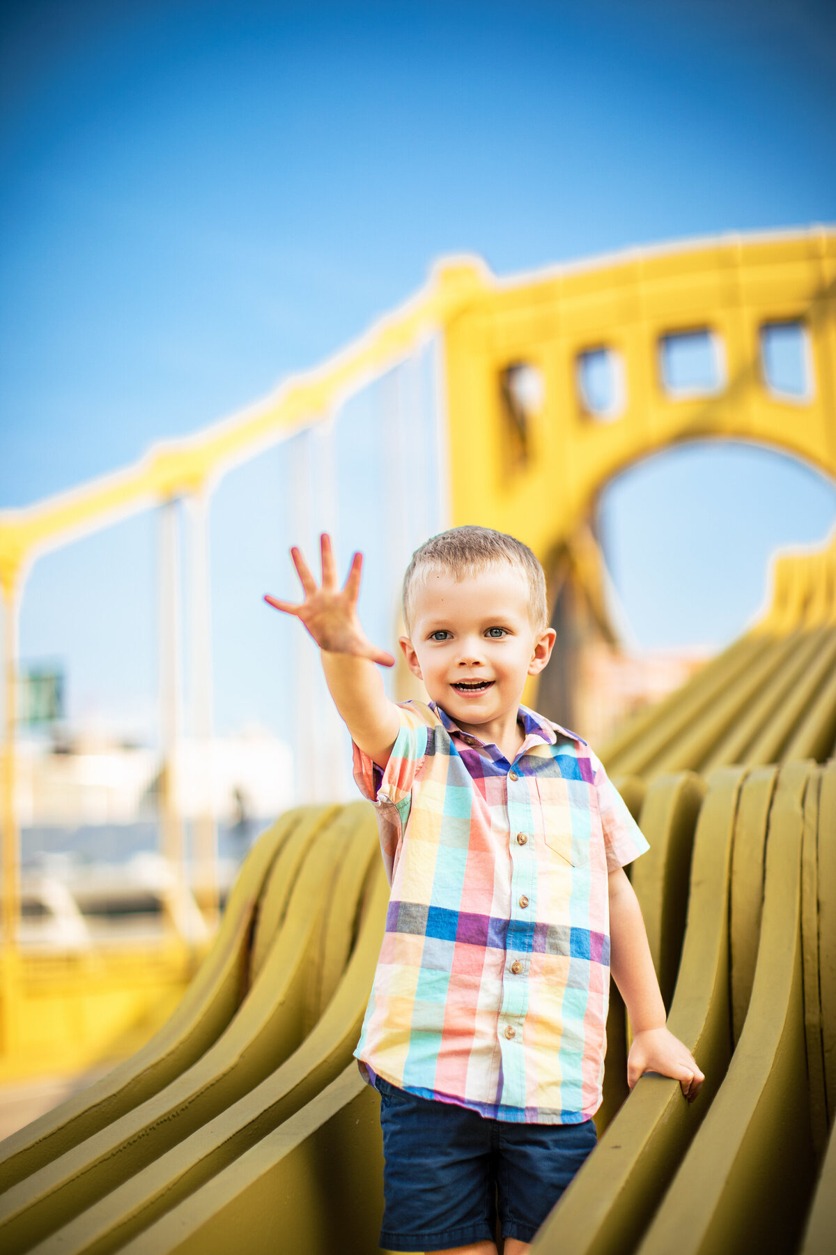 A four year old boy holds out his hand and poses for a children's portrait on one of the famous yellow bridges in Pittsburgh Pennsylvania