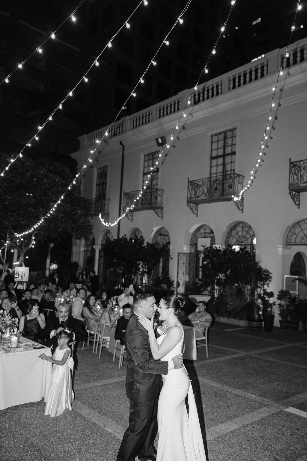 Bride and groom first dance in front of all their guests at cafe julia under twinkle lights black and whtie