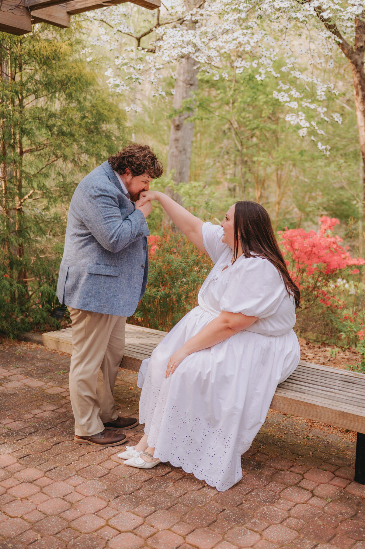 A couple gives each other a hand kiss while sitting on a park bench