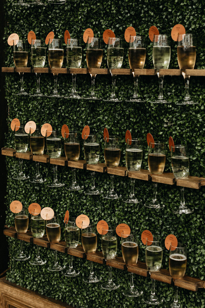Champagne flutes at  the wedding reception on a greenery wall.
