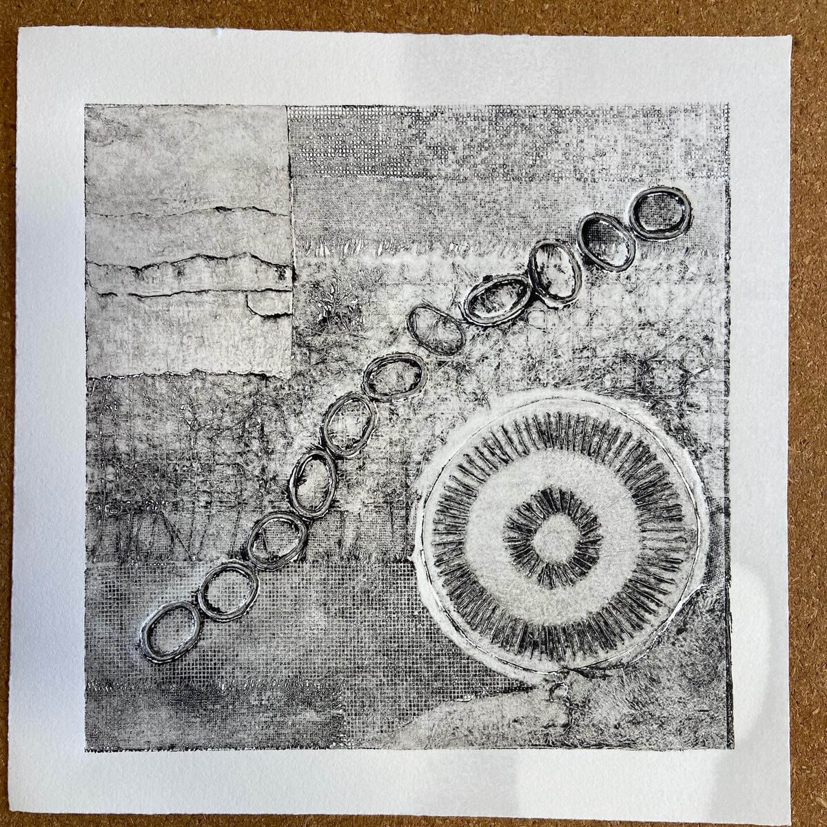 Collagraph print with a circular radiating pattern and linked oval shapes, layered over a textured background of woven and torn paper effects.