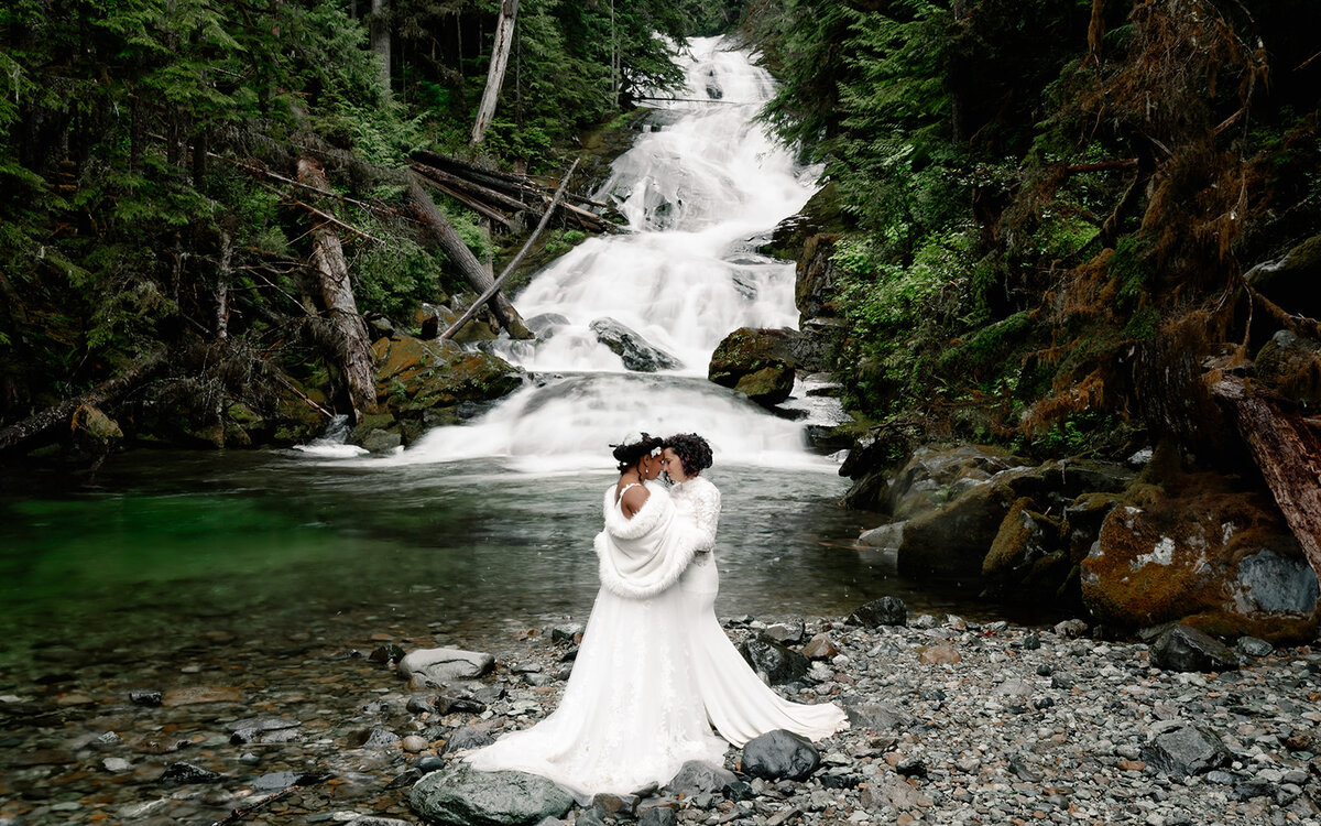 two brides embrace in front of a cascading waterfall during their adventure elopement
