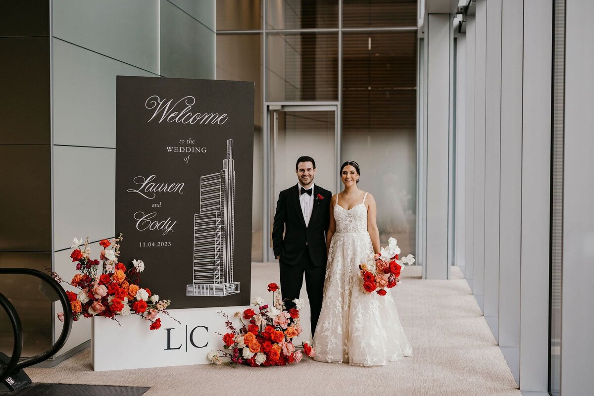 Bride and groom standing with welcome sign with florals by Philadelphia Florist Sebesta Design