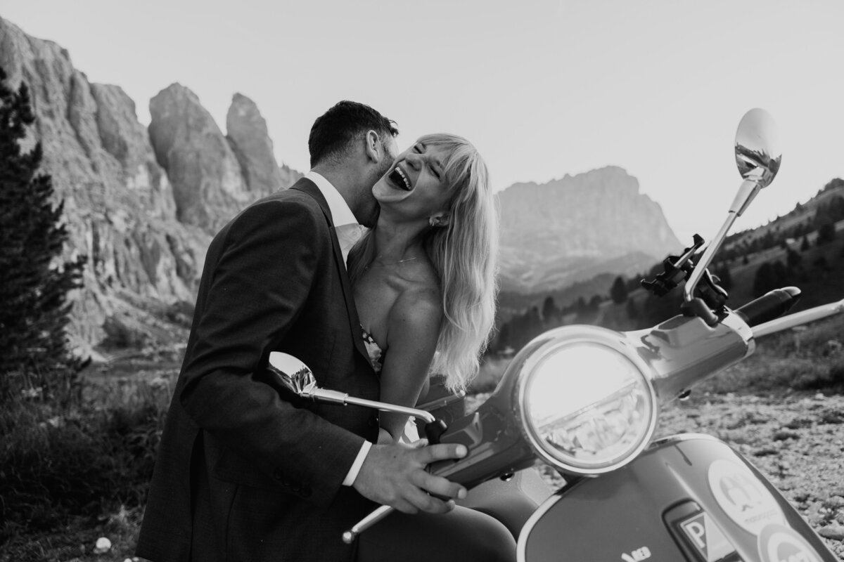 Couple laughing on red Vespa with mountain views in background