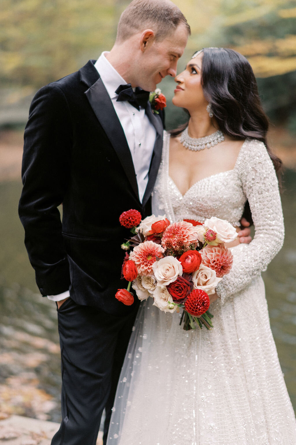 Bride and groom smiling closely together, holding a bold red and blush bouquet during their wedding at Old Edwards Inn in Highlands, NC.
