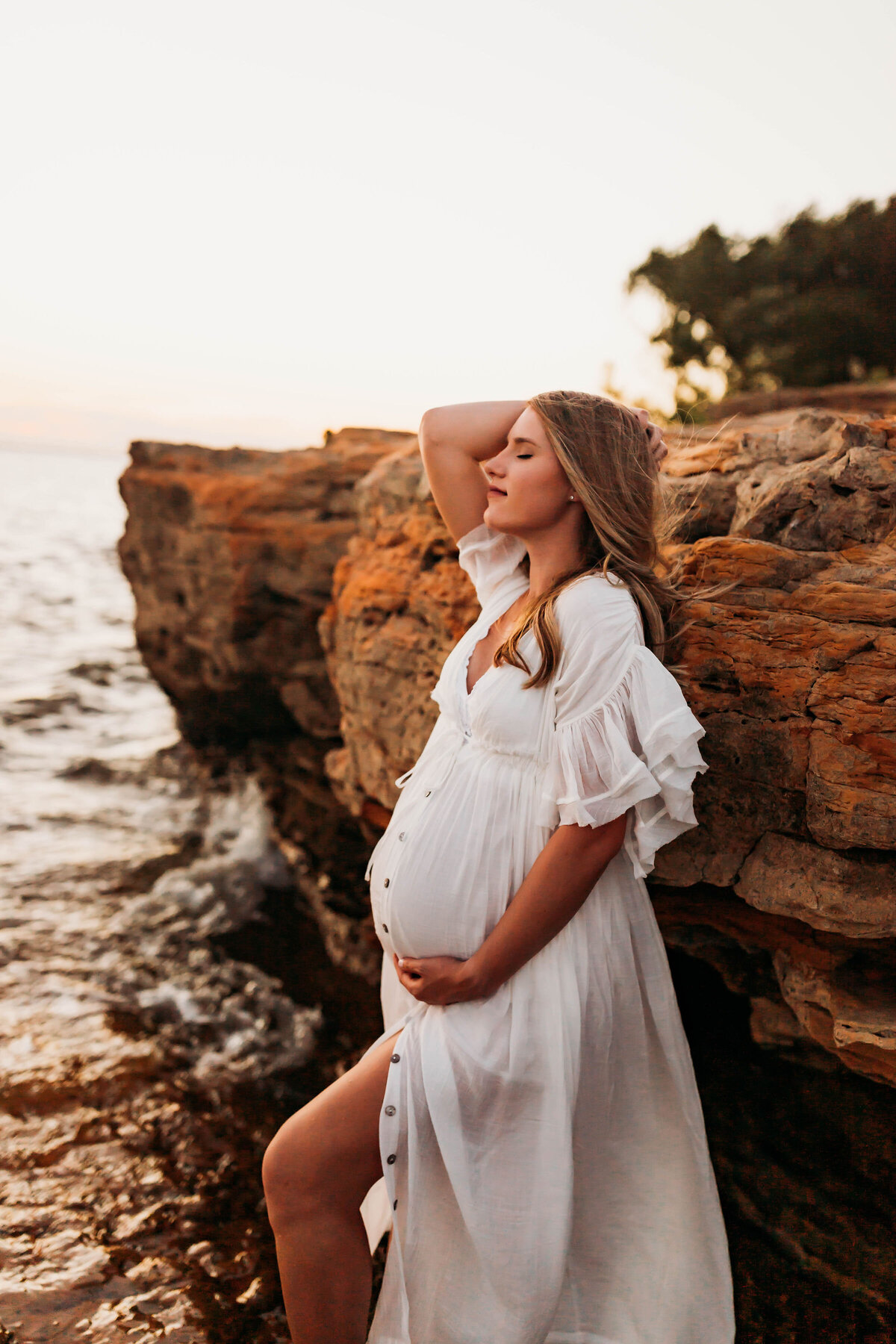 pregnant mother in a white flowy dress with windblown hair standing in the lake