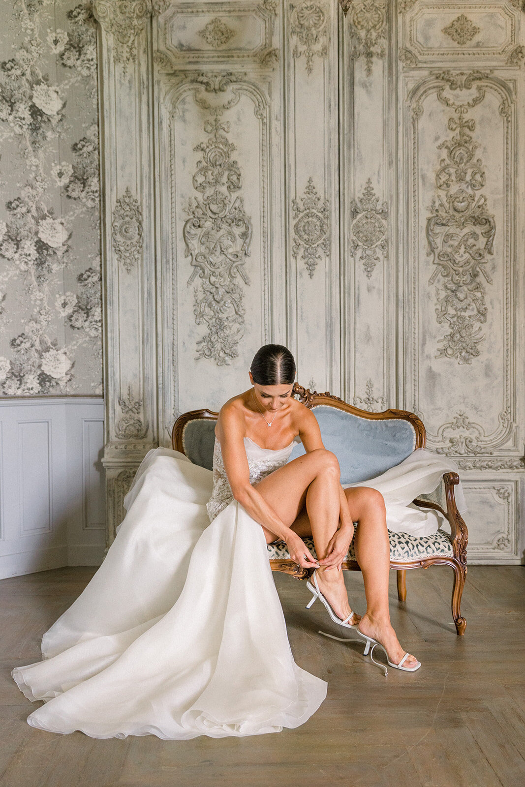 Bride putting on her shoes in a fashion-inspired, Vogue-style portrait at Château Challain, captured in elegant, natural wedding photography.