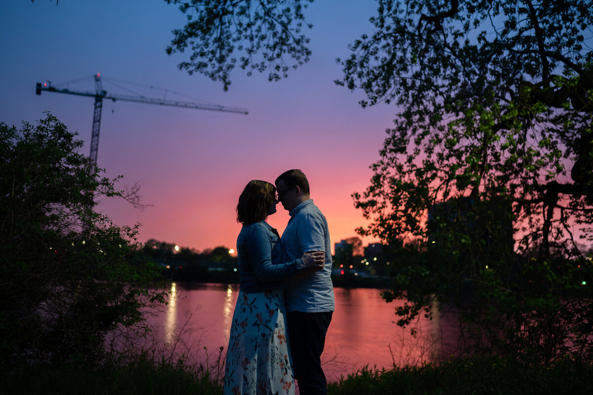 A Pink cotton candy sunset  falls behind a couple and pond