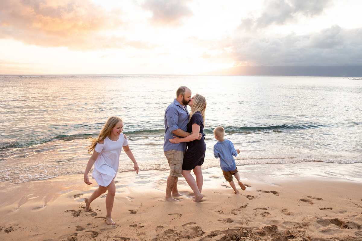 Maui Family Photographers capture mother and father kissing on beach during family beach photos in Maui