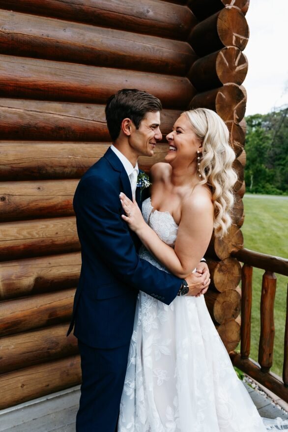 Bride with white strapless dress and curled blonde hair is held by her groom in a navy suit as they laugh together at their minneapolis wedding
