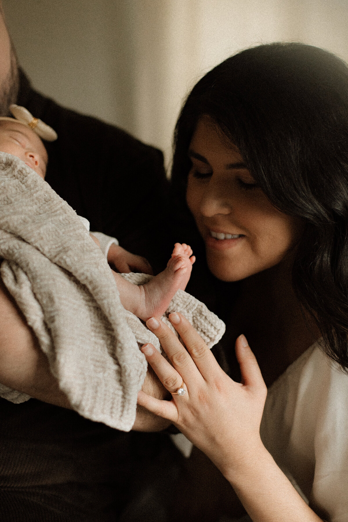 A mother gently touching her newborn’s foot with a soft smile, the baby wrapped in a textured blanket.