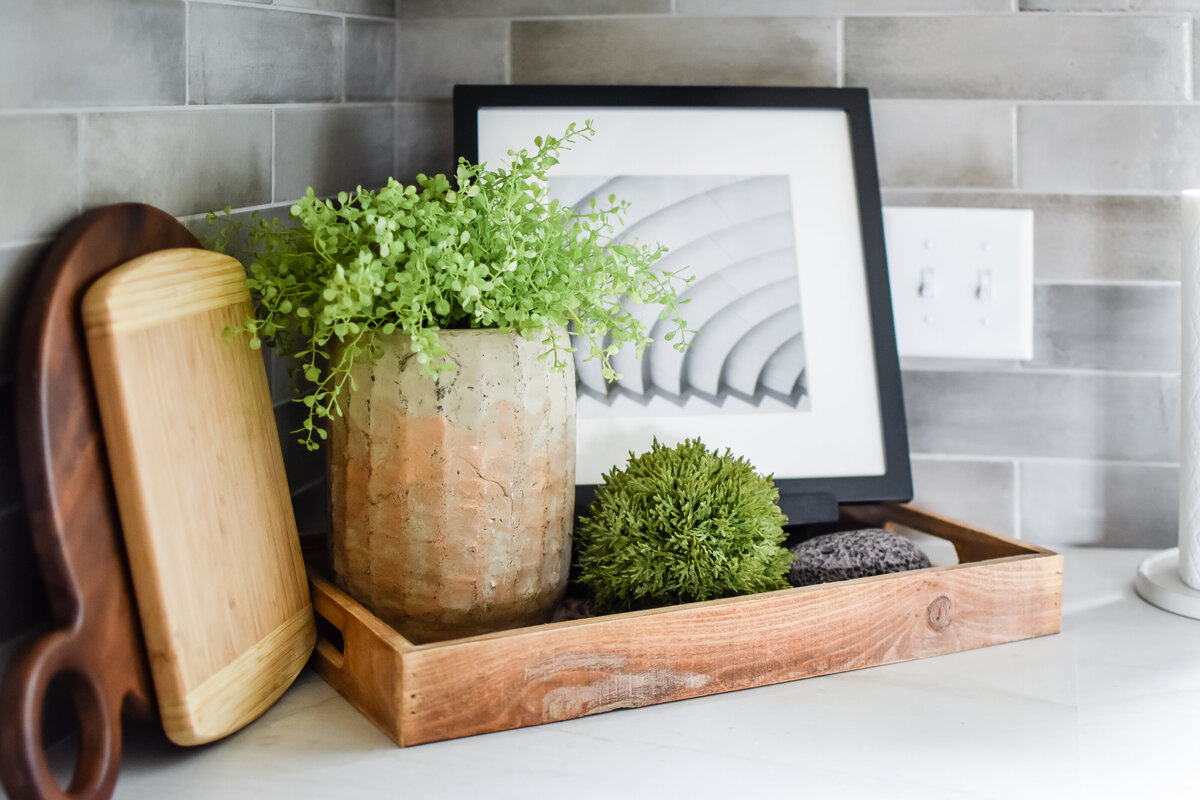 Cutting boards, a plant, and a framed photo sitting on a wood tray on a kitchen countertop
