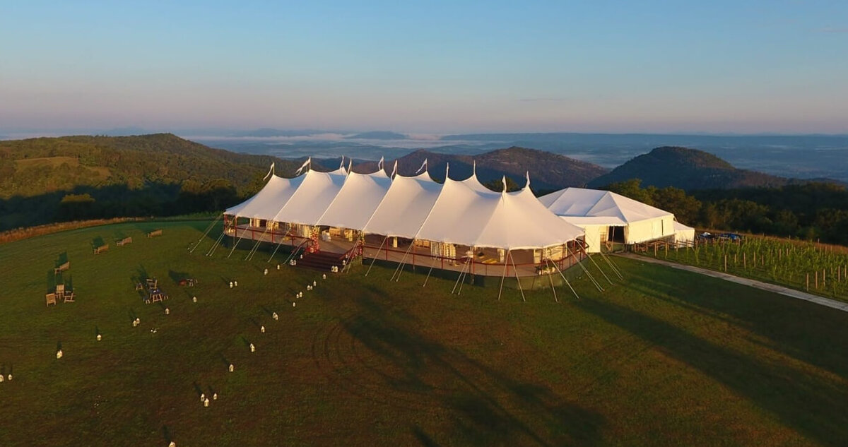 A large double pole marquee sitting on top of a hill with a view of the land below.