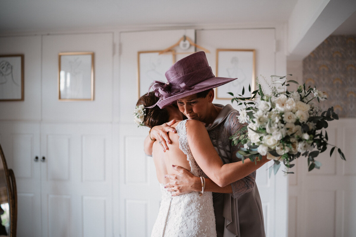 Bride and her mother share an emotional hug in the bridal suite at Broadfield Court, Herefordshire, with a soft bouquet and elegant wedding dress.