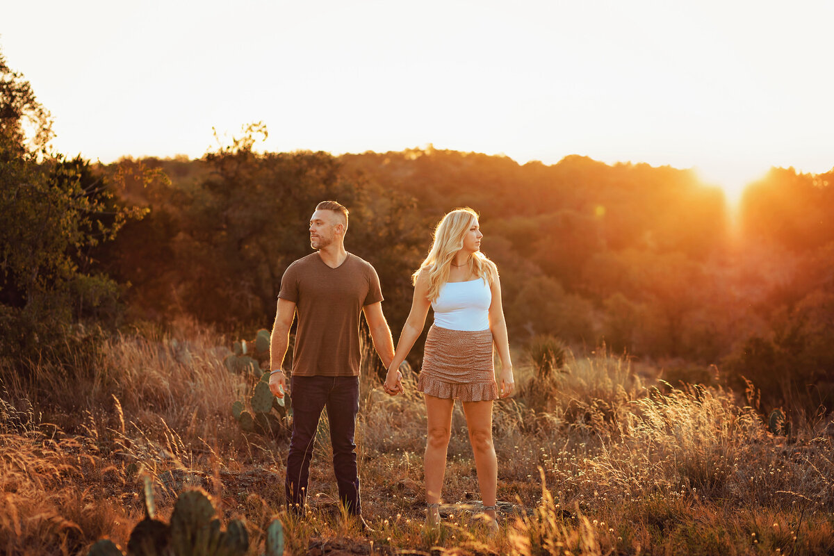 Adorable couple in casual attire stand in a wide open field at sunrise during their texas engagement session.
