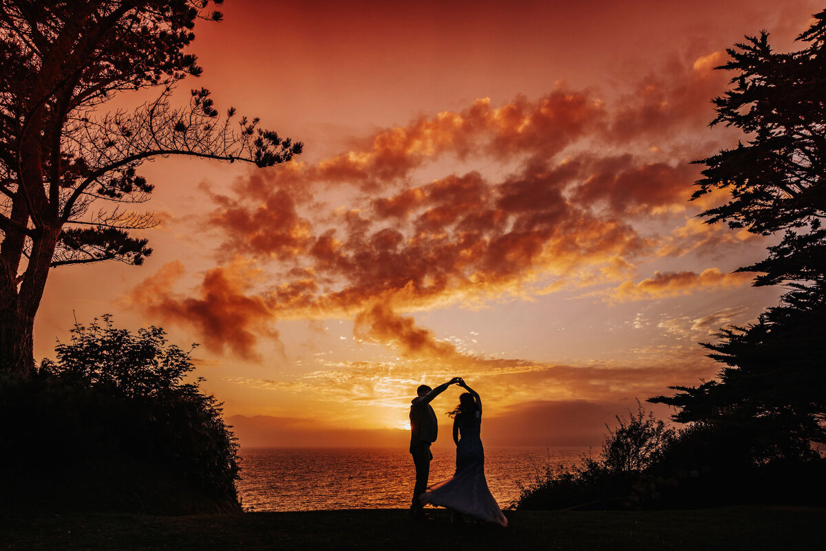 A bride and groom are silhouetted against a sunset