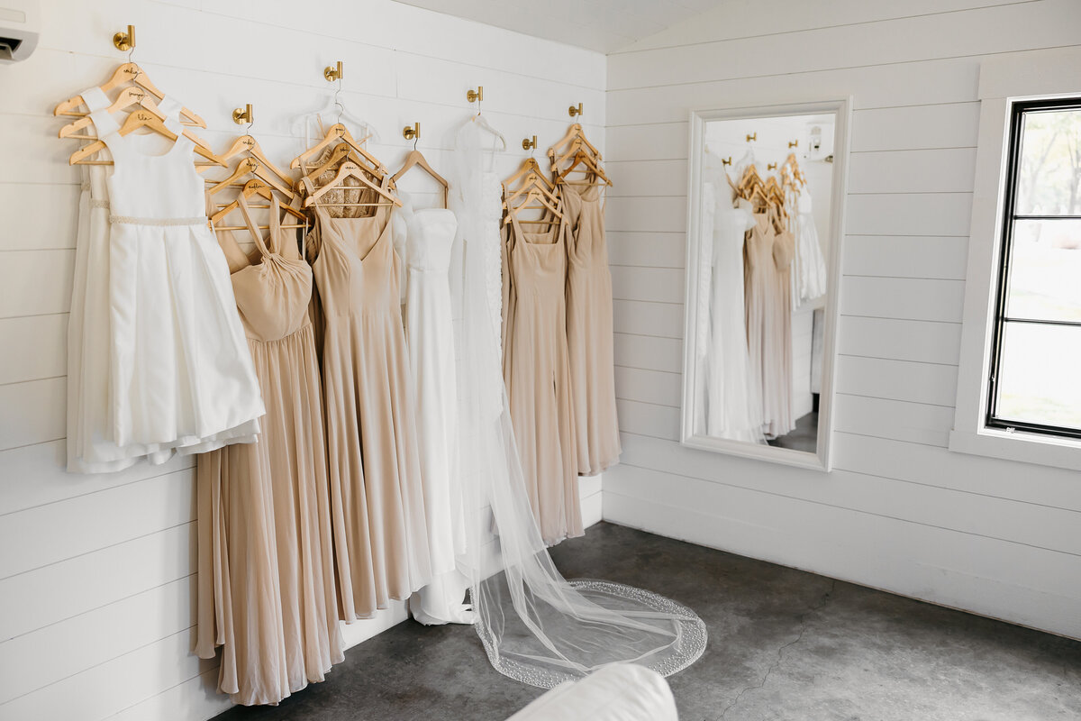 Wedding dress and bridesmaid dresses hanging against white wall