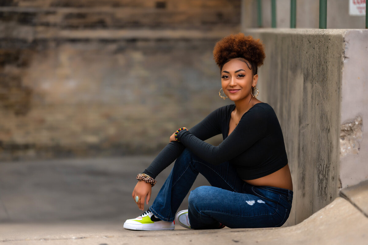 A student from Kettle Moraine High School is seated along a short concrete wall in Downtown Waukesha while posing for her senior portrait.