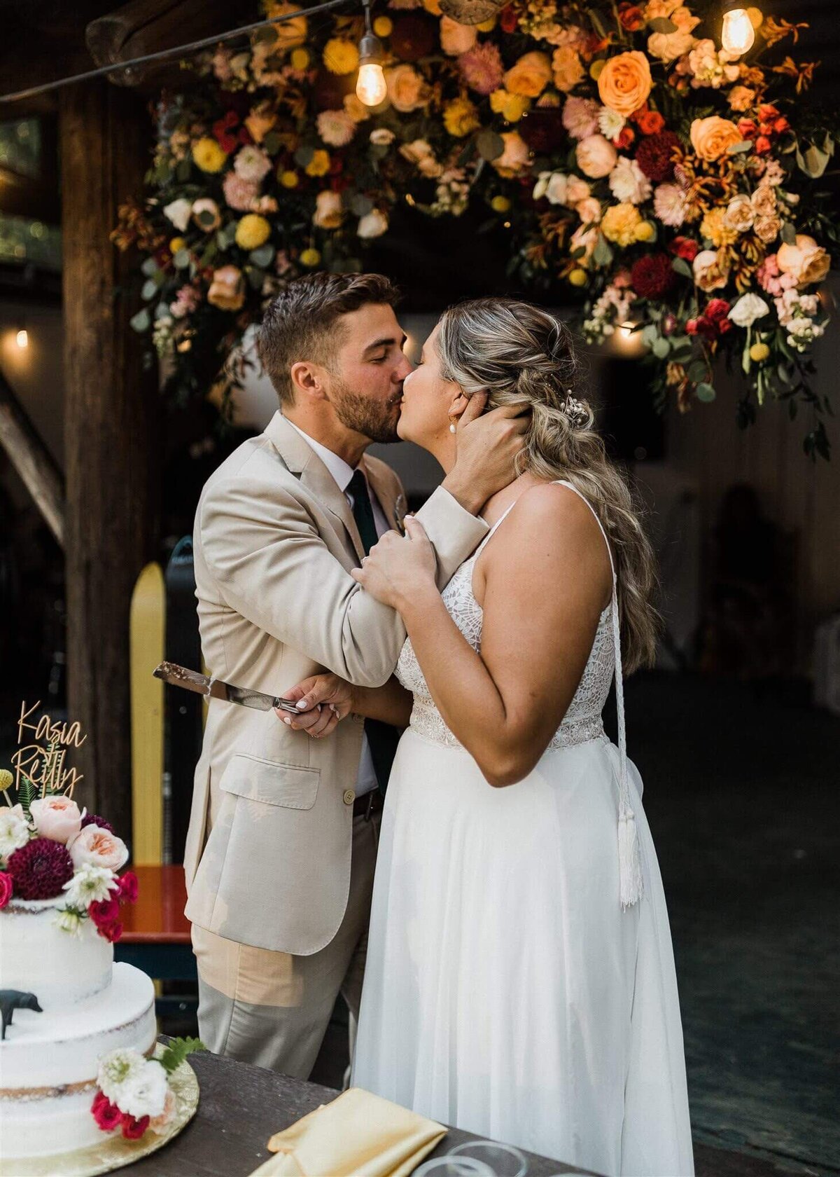 Bride and groom kiss during their reception with large floral installation behind them.