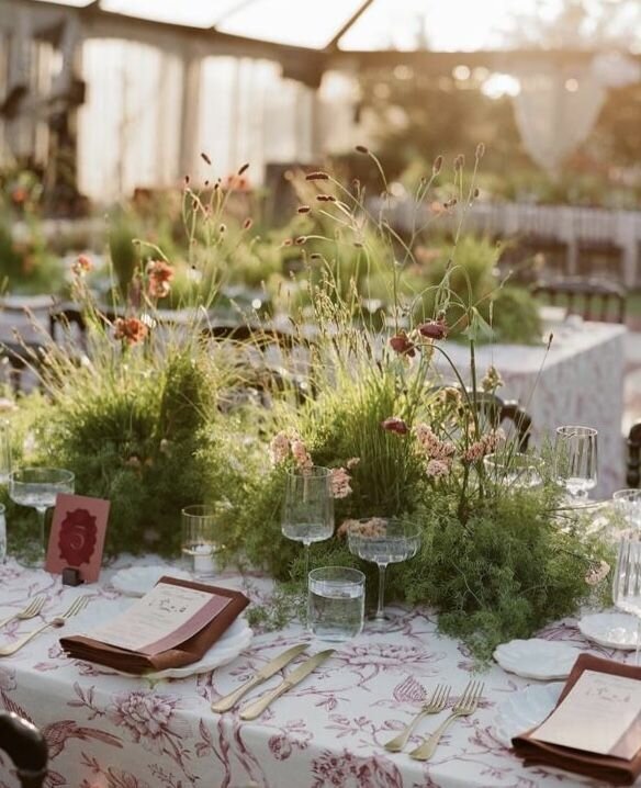 Playful wedding tablescape with greenery and floral linens, a look we'd translate into a Wrightsville Manor reception design