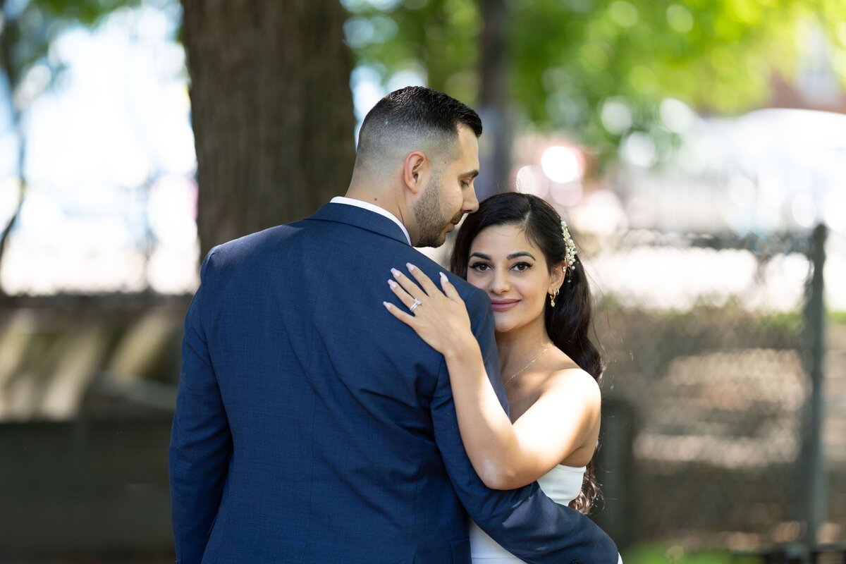 The groom lovingly holds his bride as she gazes directly at the camera. This photo captures their joyful connection and showcases their happiness and love during their wedding celebration.