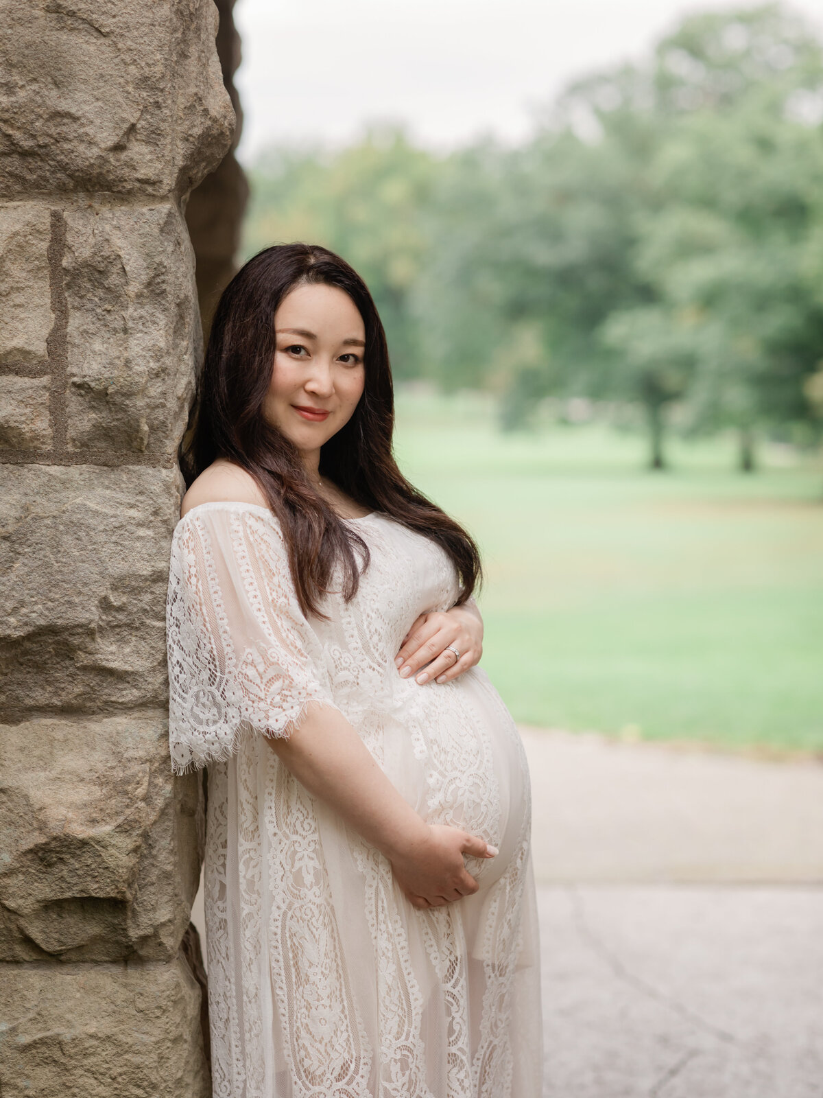 pregnant mother in white lace gown holding belly for maternity portraits 