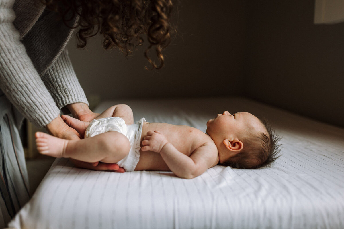 newborn in diaper laying on bed looking up at mom changing her diaper