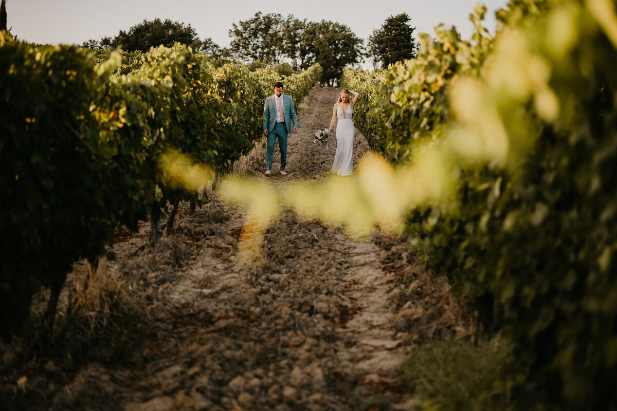 Bride and groom walking hand in hand among the vineyard rows at Borgo Divino, romantic wedding in Tuscany.