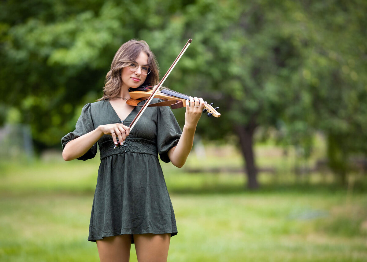 high school senior girl in green dress plahing her violin outside