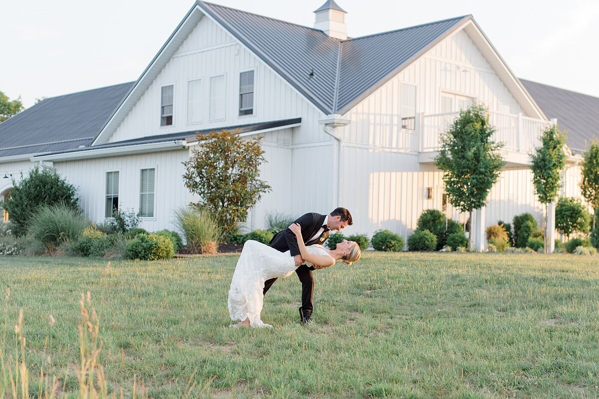 Magnolia Hill Farm wedding venue in the background while the groom dips his bride in front of the venue on the lawn as they laugh together