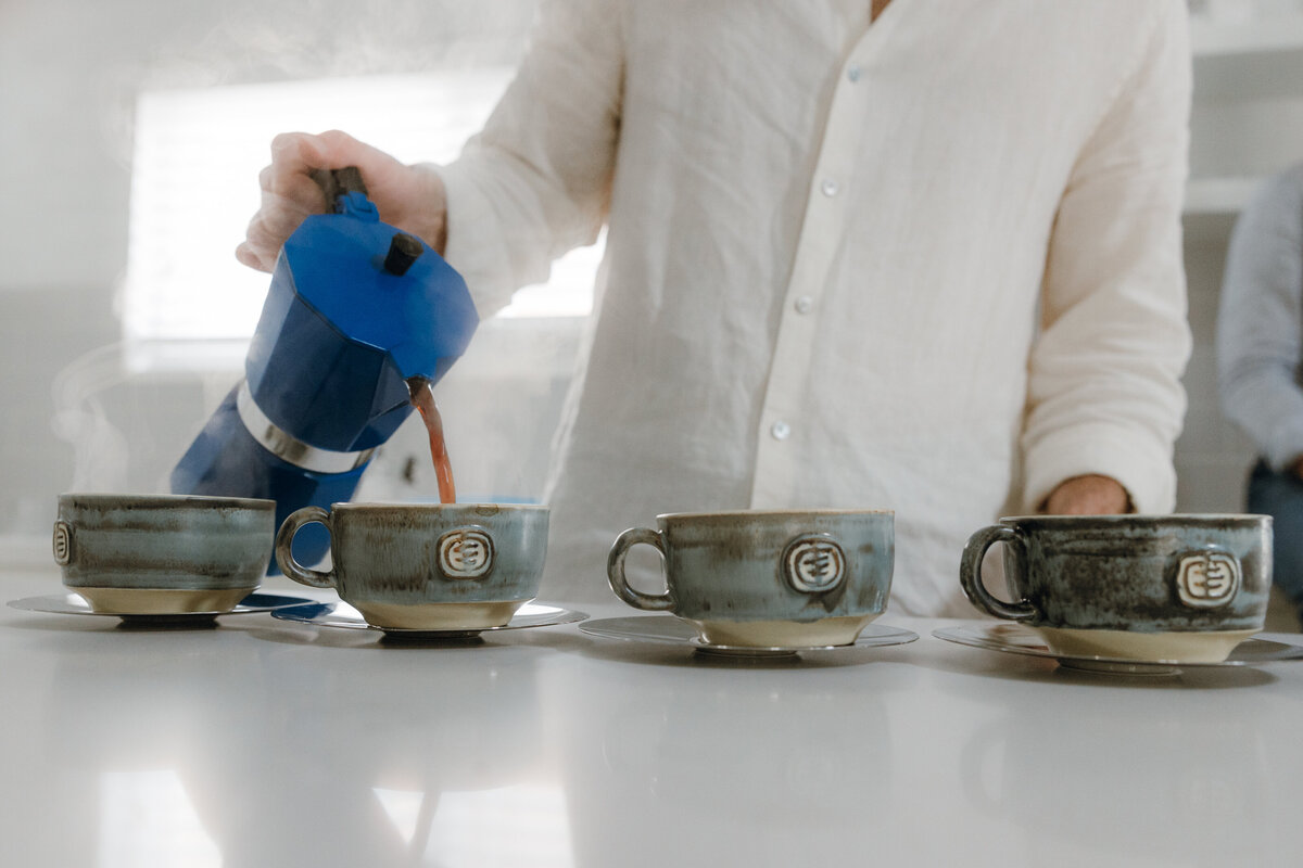 4 mugs and a man pouring coffee from a blue moka pot.