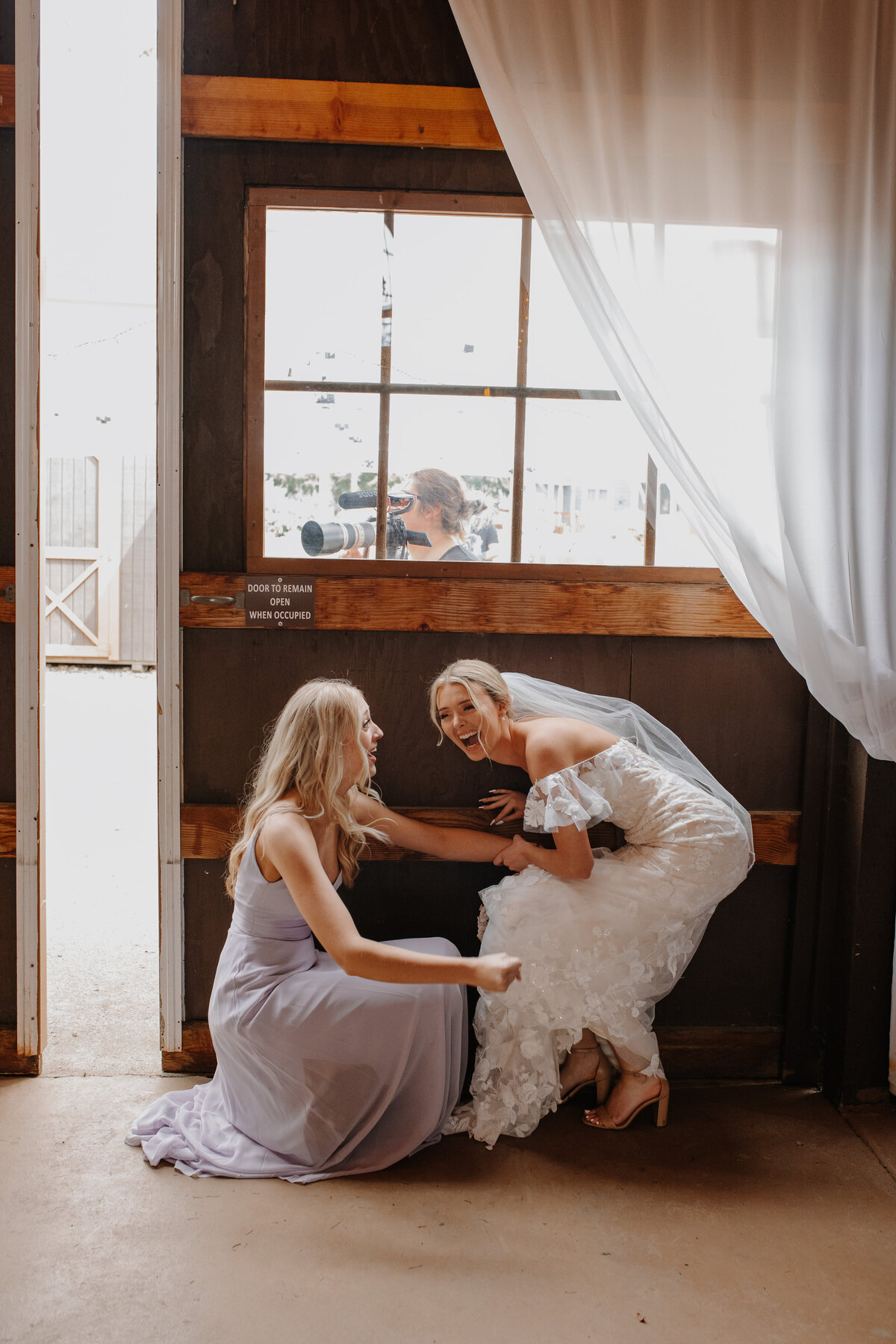 Bride and bridesmaid crouched beneath window