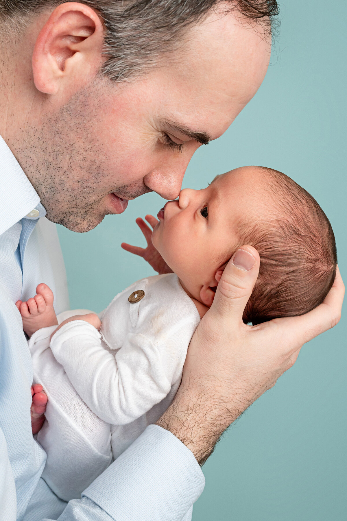dad holding his newborn baby boy up close in a way that looks like the baby is kissing his nose