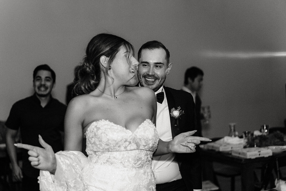 In a black-and-white photo, the bride and groom dance happily together, with the groom grinning and the bride animatedly enjoying the moment.