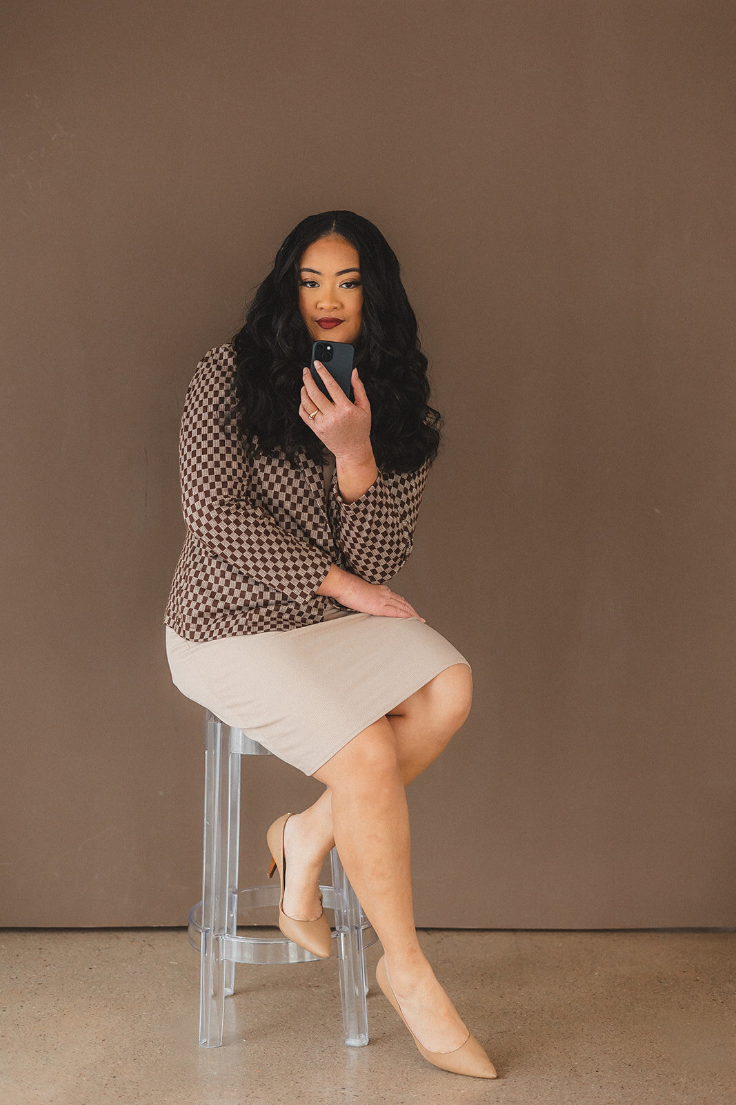 A woman sitting on a stool, casually using her phone with a relaxed expression.